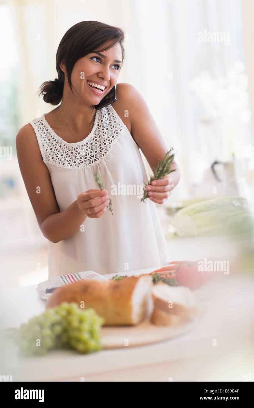 Hispanic woman talking on cell phone and cooking in kitchen Stock Photo