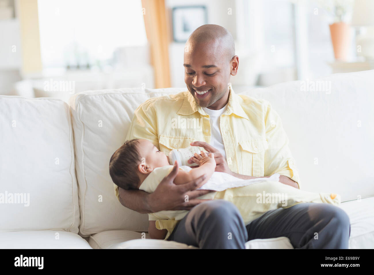 Smiling father feeding baby on sofa Stock Photo