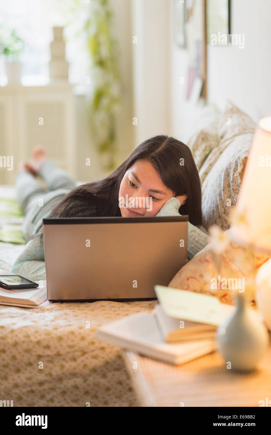 Mixed race teenage girl doing homework on bed Stock Photo Alamy