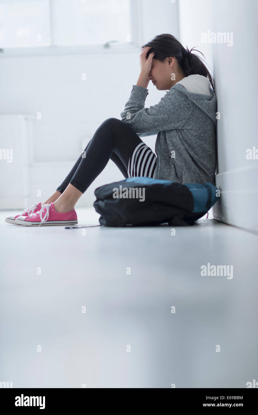 Mixed race teenage girl covering her face in school hallway Stock Photo