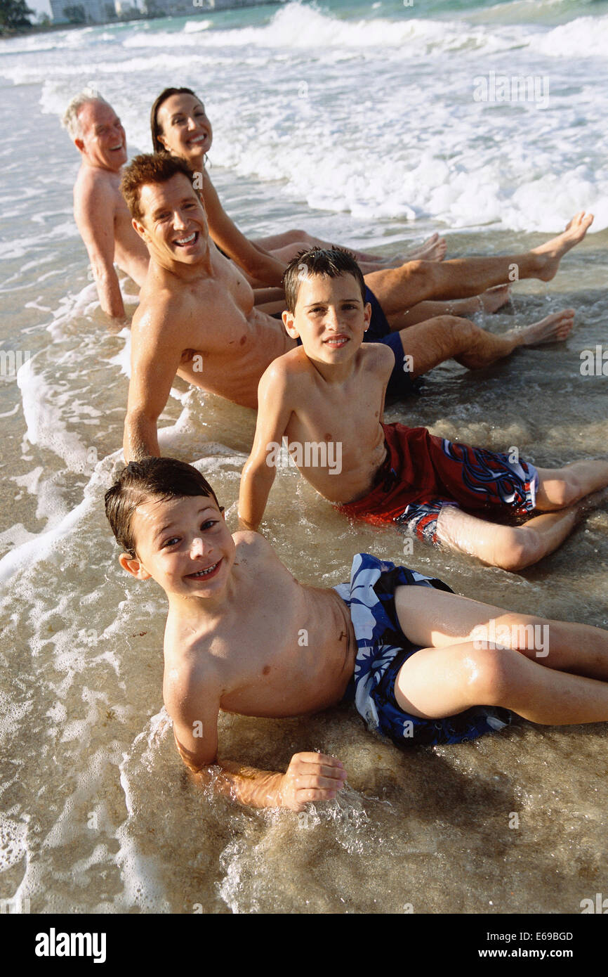 Family sitting in waves on beach Stock Photo
