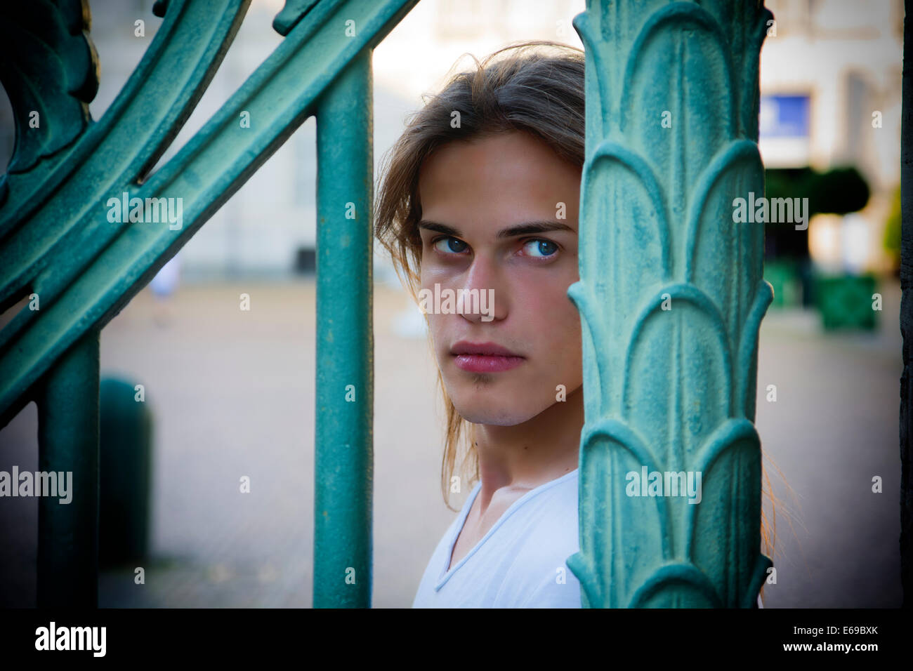 Gorgeous Long Hair Man in White behind Blue Green Art Metal Bars Stock Photo