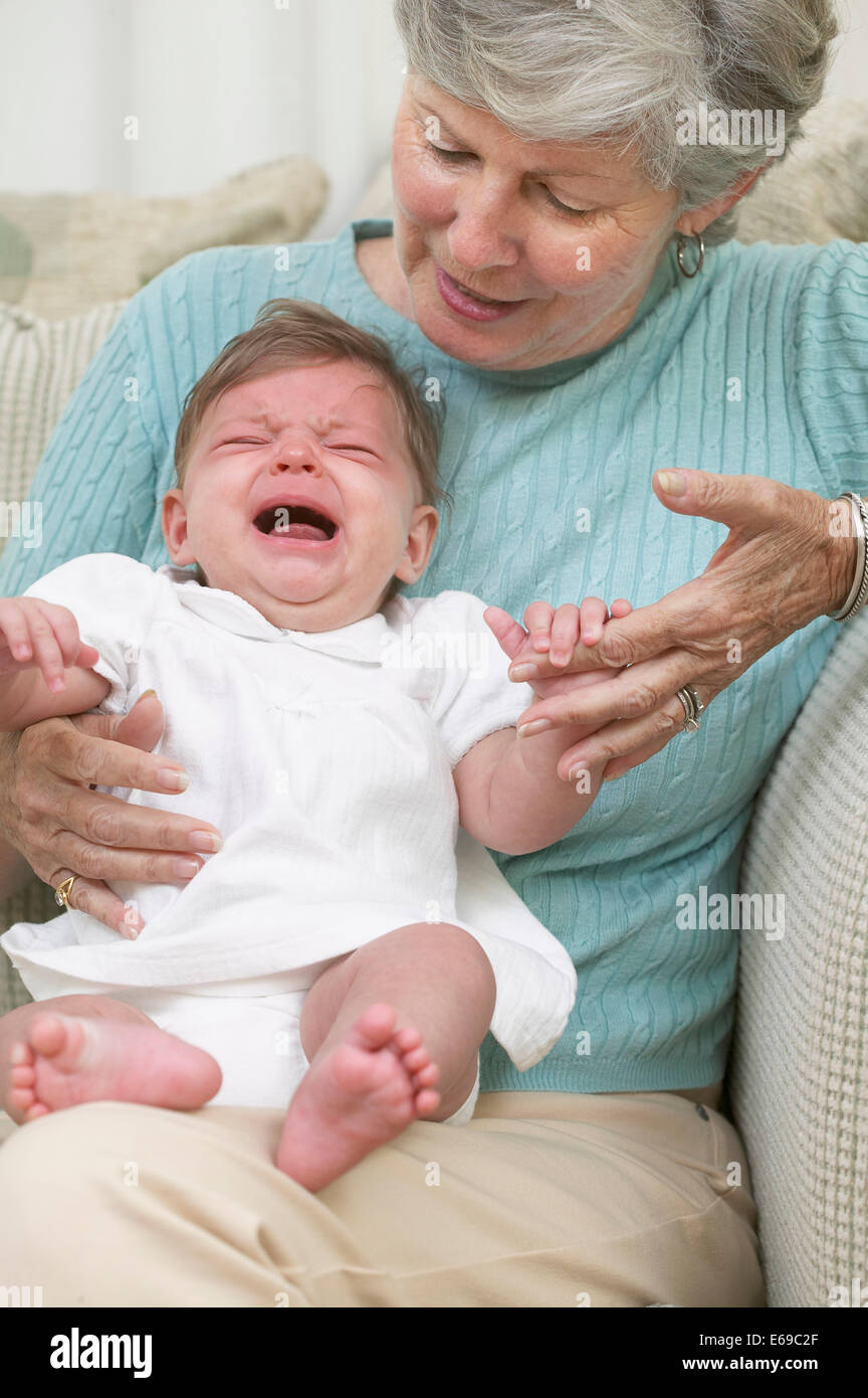 Senior woman with crying granddaughter on sofa Stock Photo