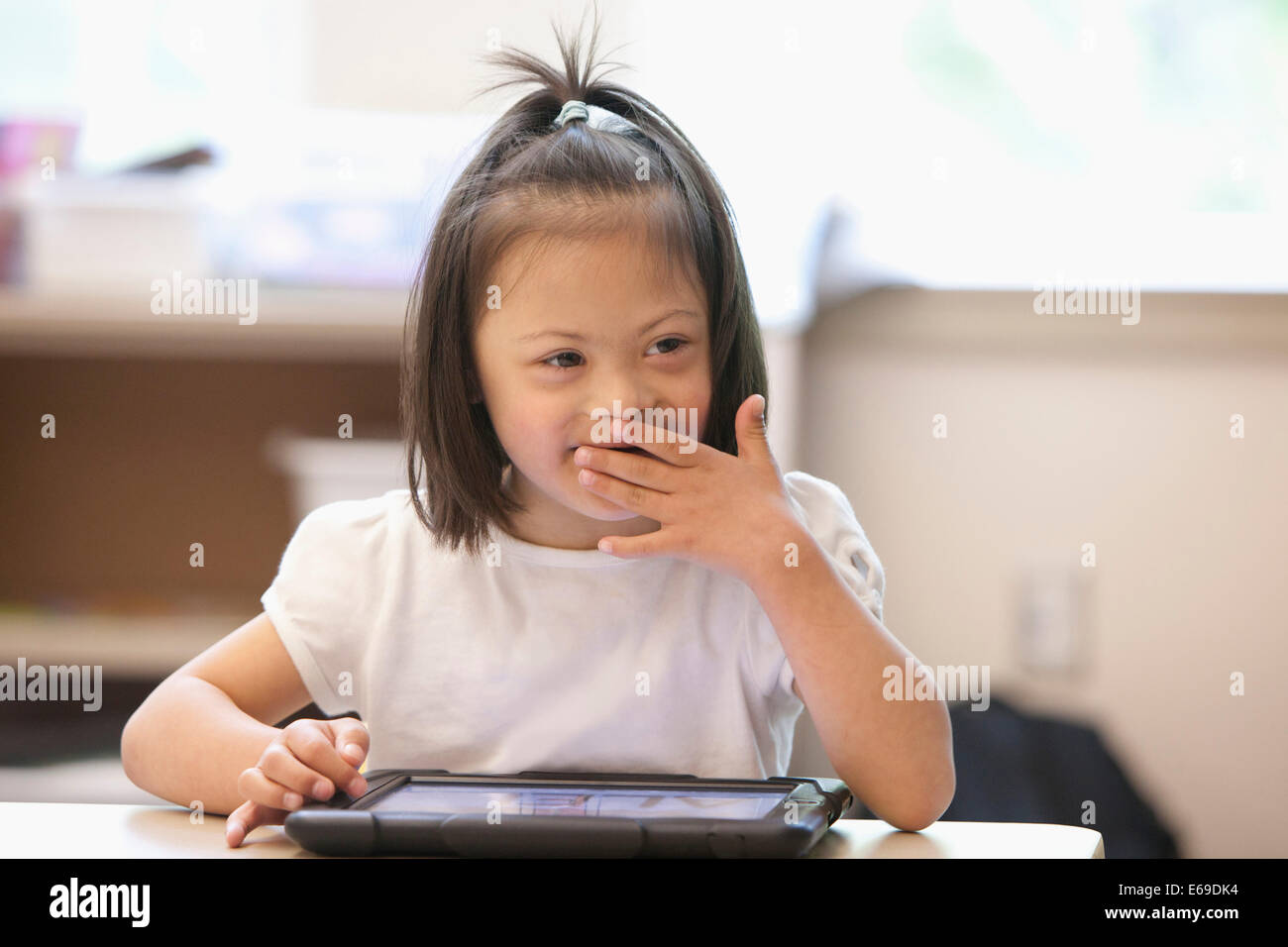 Mixed race Down syndrome student using tablet computer in classroom Stock Photo