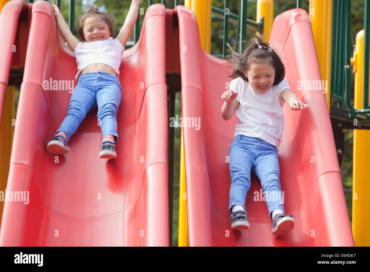 Mixed race boy sliding down slide in playground - Stock Photo - Dissolve