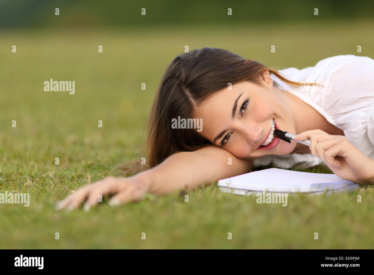 Candid happy woman lying on the grass writing with a green unfocused background Stock Photo