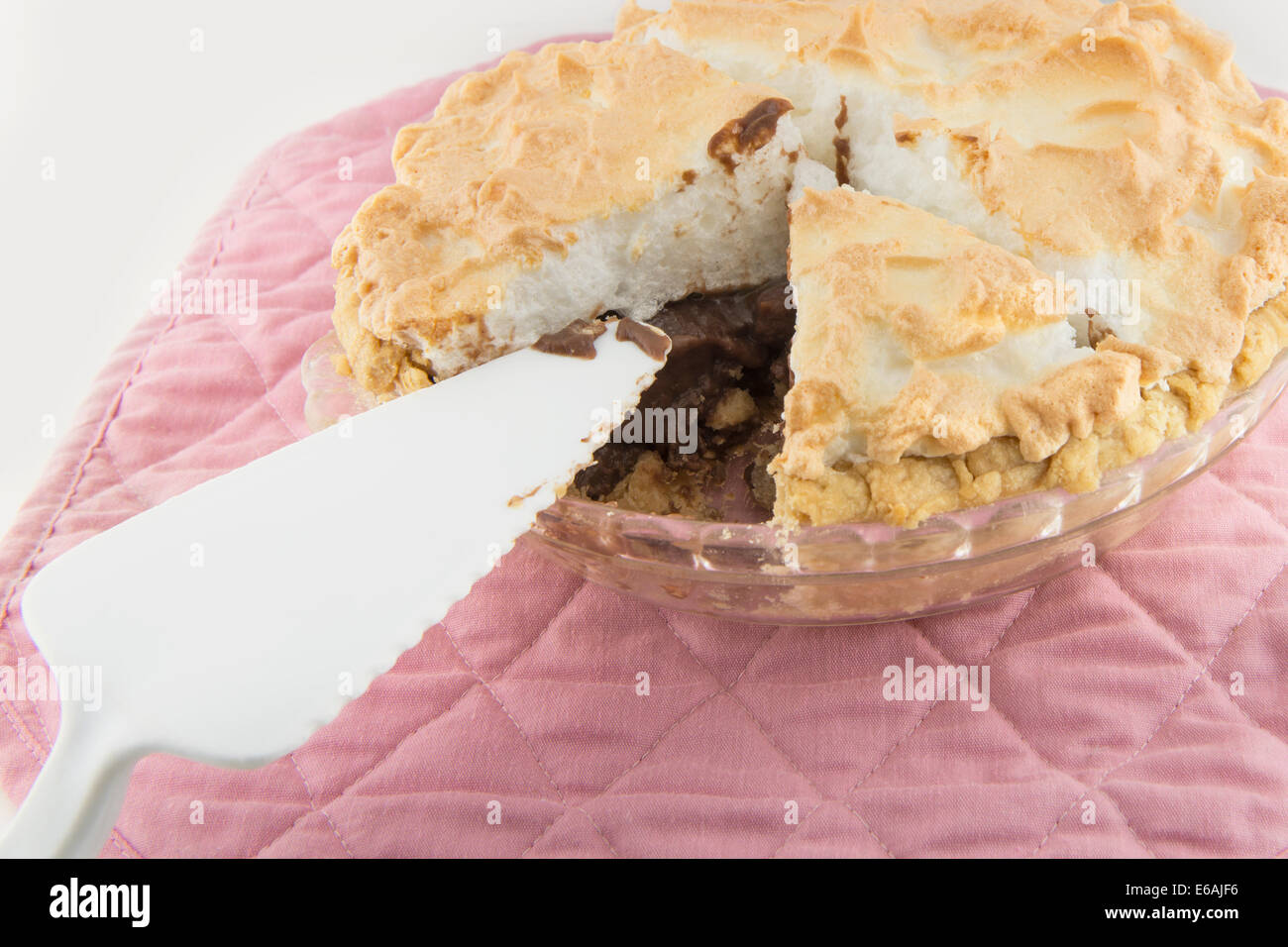 A home made chocolate meringue pie with one piece gone, pictured with a serving utensil on a pink mat. Closeup. USA. Stock Photo