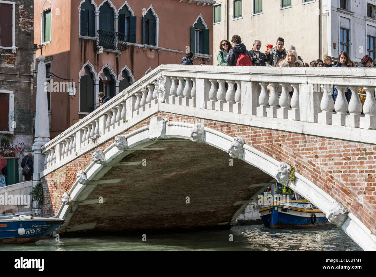 Tourists crossing a bridge decorated with faces over one of the side canals of Venice. Stock Photo