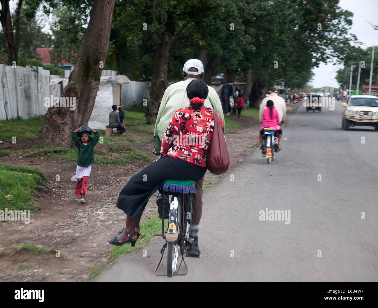 Bicycle taxi giving lift to well dressed black African young woman riding side saddle on outskirts of Nakuru town Kenya Stock Photo