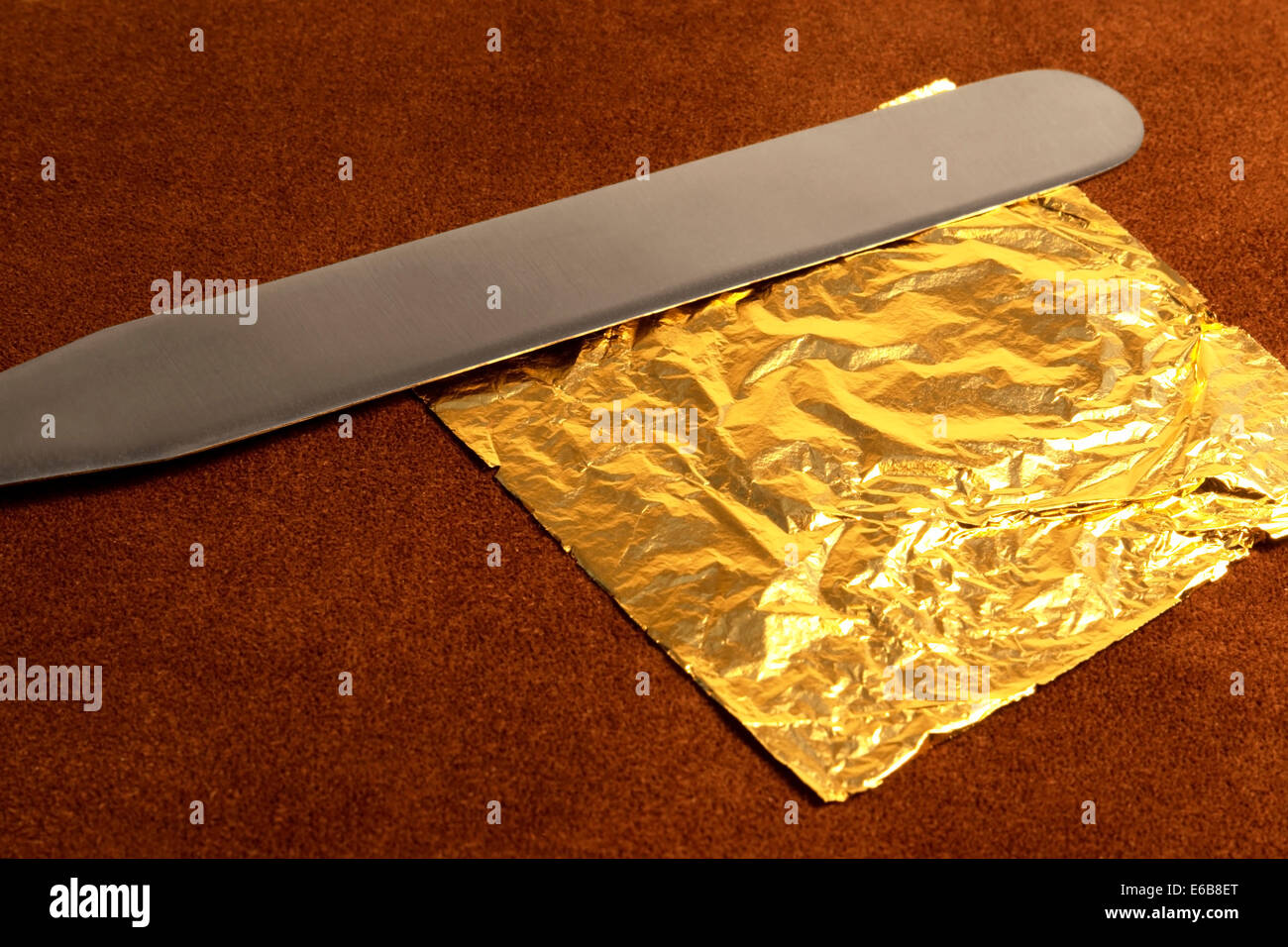 gilding theme with a leaf of beaten gold and blade on brown leather surface in warm ambiance Stock Photo