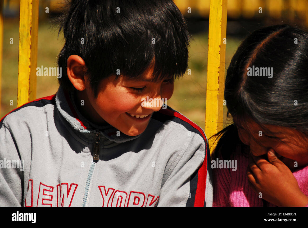 Bolivia, El alto, close-up of a small boy and girl sitting by pole, looking at each other and smiling. Stock Photo