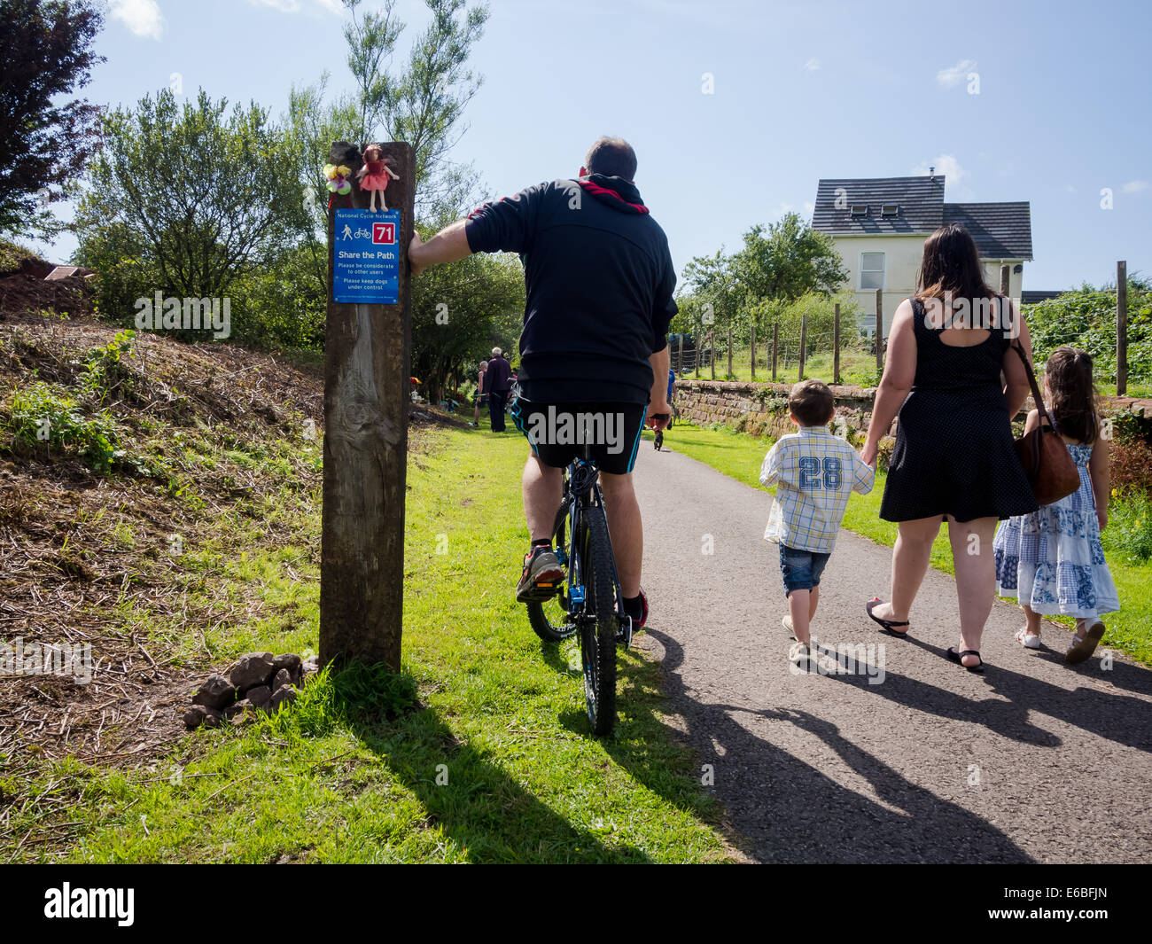 A cyclist passes a walking mother and two children on the coast to coast cycle route in Moor Row, Cumbria, England Stock Photo