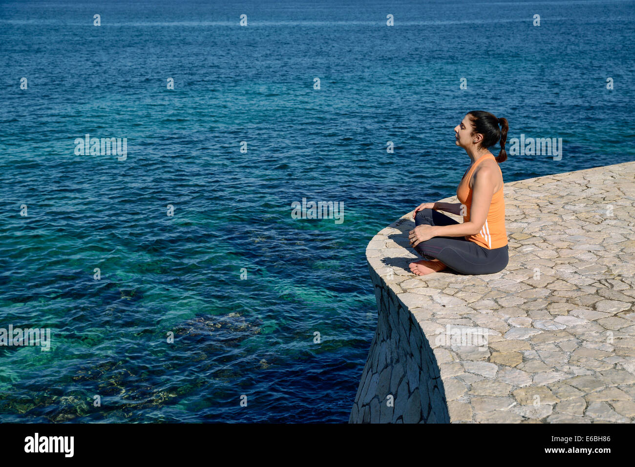 Woman practicing oceanfront yoga meditation. Stock Photo