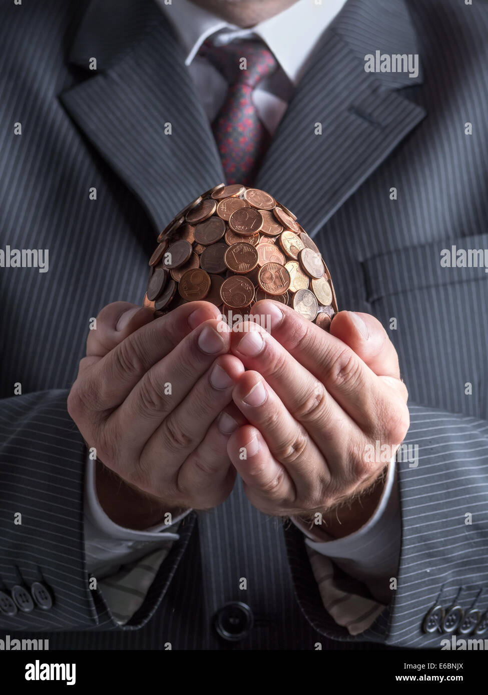 Businessman wearing suit holding one eurocent egg in his hands Stock Photo