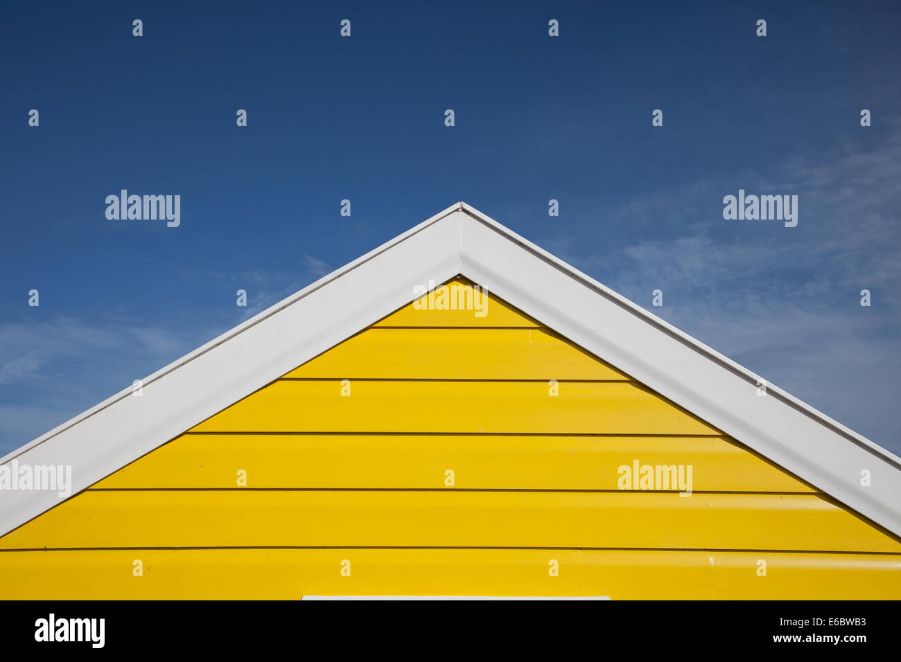Yellow beach hut against blue sky, the roof apex is pointing up into the sky Stock Photo