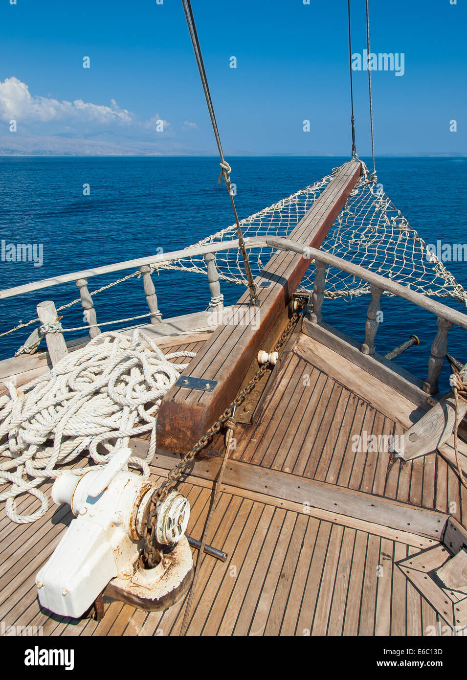 the bow of a traditional wooden boat with teak deck, hardwood bowsprit with blue sea and blue sky behind Stock Photo