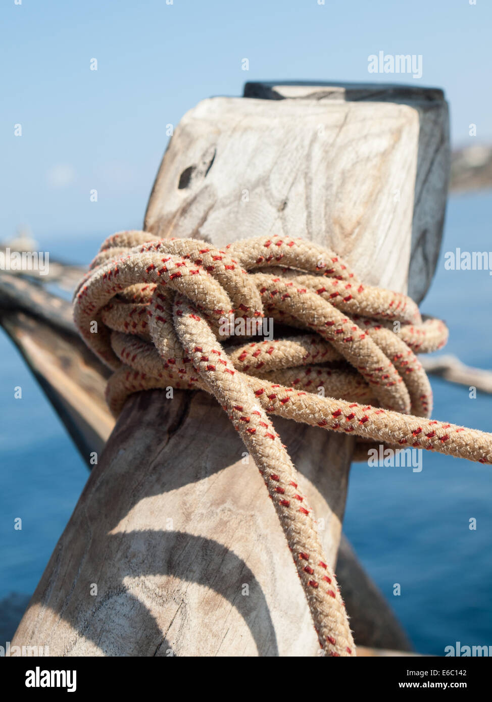 detail of ships rope tied off on a wooden bollard with sea behind Stock Photo