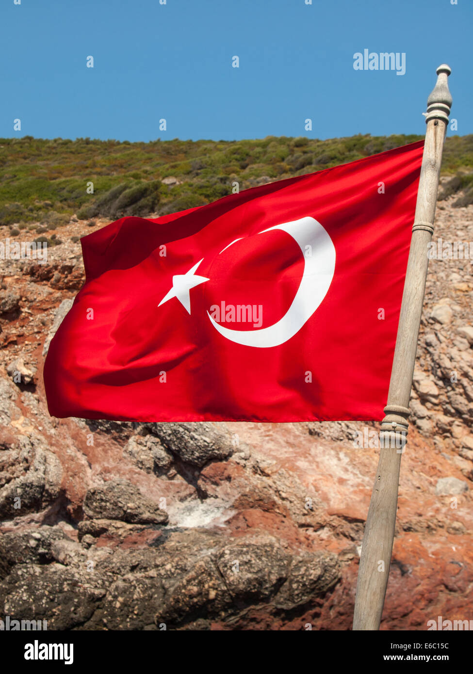 turkish flag on a hardwood mast flying in a strong wind with rocky coast and blue sky behind Stock Photo
