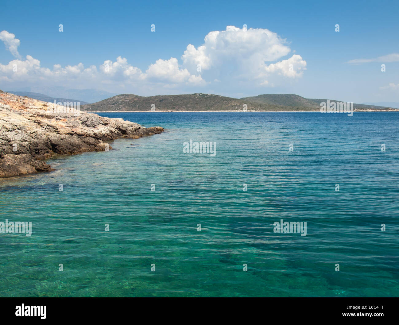 rocky coastline with green sea, blue sky and hills behind Stock Photo