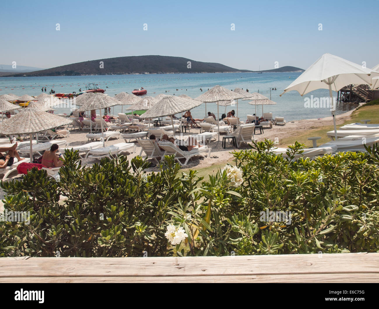 Cesme, Turkey,  August 2nd, 2014: Tourist beach on the Cesme peninsula in high season viewed through palm trees. Stock Photo