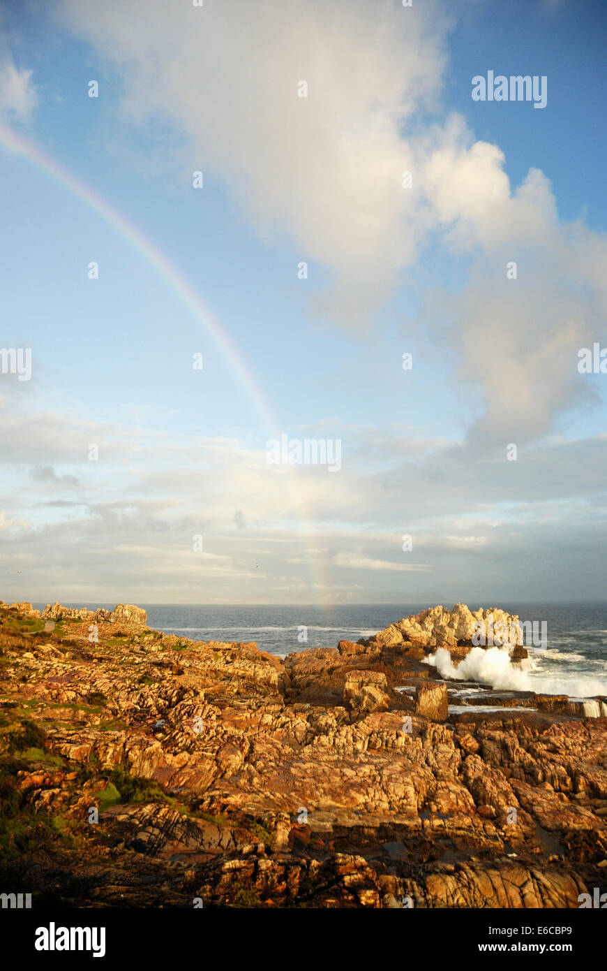 Rainbow and waves breaking on rocky shore at sunset, Hermanus, South Africa Stock Photo