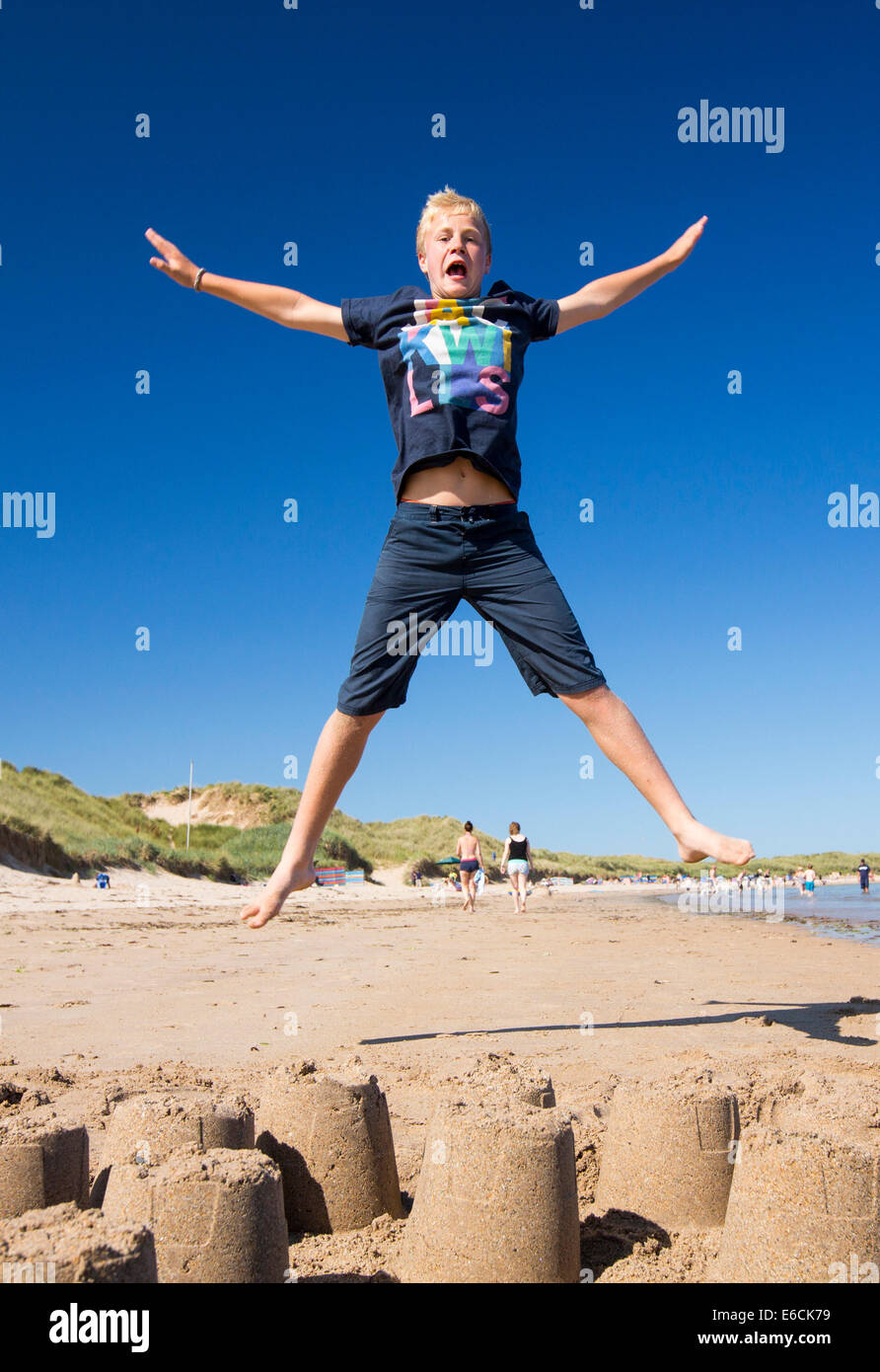 A boy jumping over a sandcastle on Bamburgh Beach, Northumberland, UK. Stock Photo