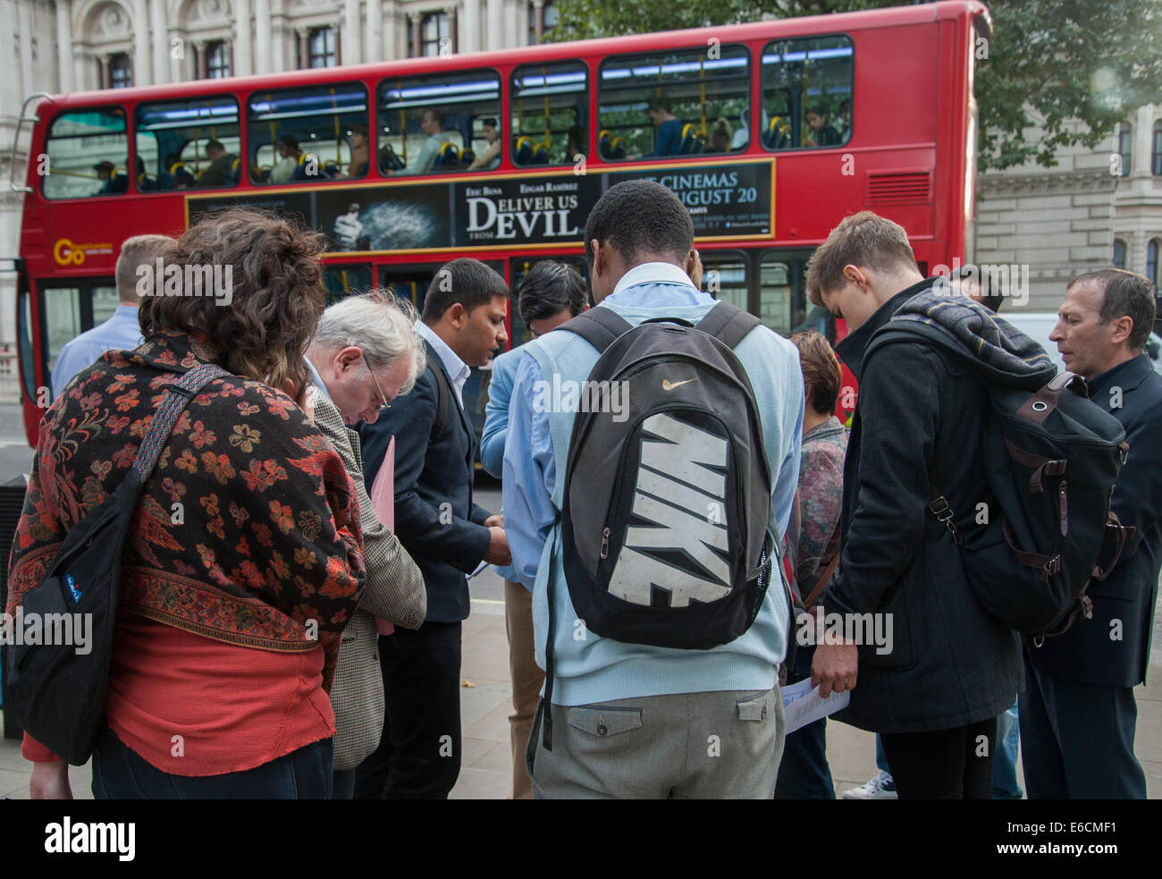 London, UK. 20 August, 2014. A small group of Christians including Catholics and Baptists gather opposite Downing Street to hold prayers for journalist James Foley, murdered by ISIS, as well as peace in Iraq. A poster on a bus behind them reads, 'Deliver Us from Evil.' Credit:  Pete Maclaine/Alamy Live News Stock Photo