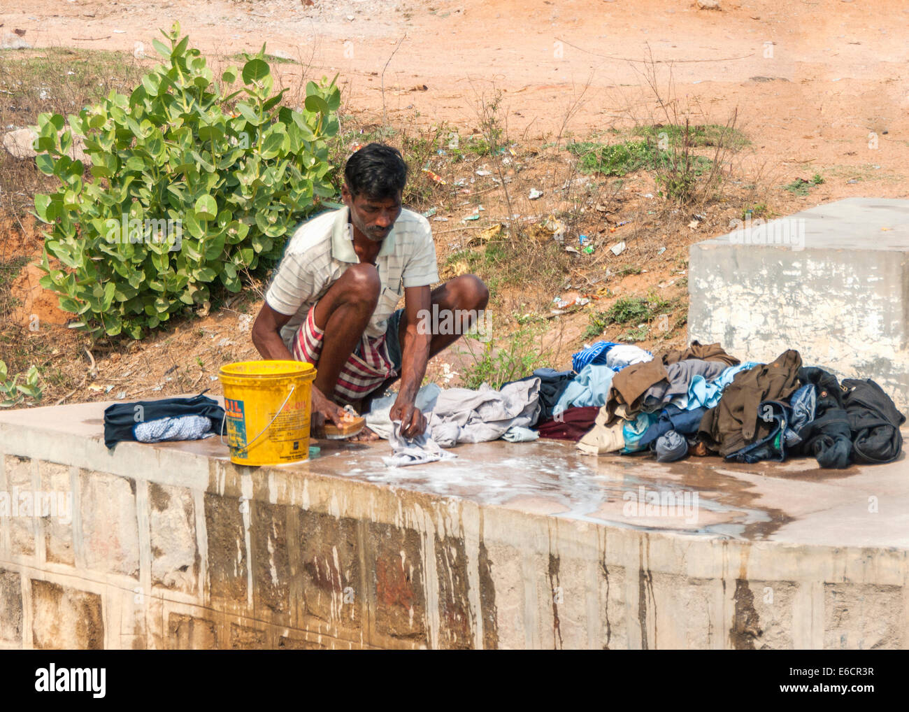 Man does laundry manually on the concrete slab of river bridge, using ...