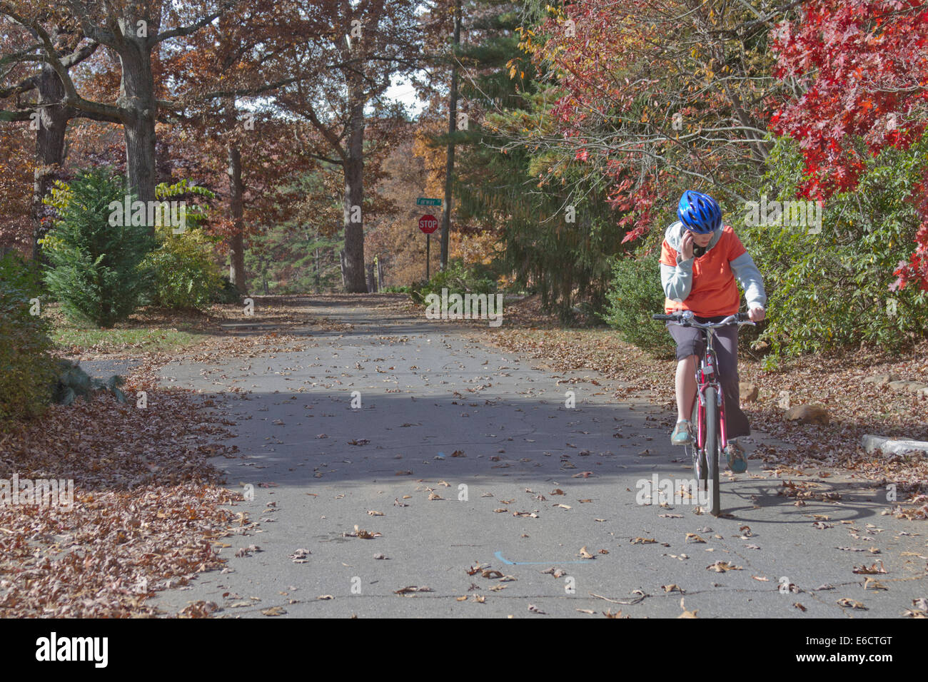 Young woman talking on a cell phone while riding a bike and not paying attention to the beautiful autumn landscape around her Stock Photo