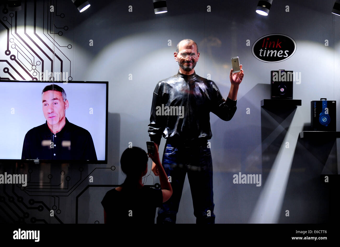 Shenyang, China's Liaoning Province. 18th Aug, 2014. A pedestrian takes photos for a wax statue of Steven Jobs at a store selling Apple phones in Taiyuan Street in Shenyang, northeast China's Liaoning Province, Aug. 18, 2014. © Zhang Wenkui/Xinhua/Alamy Live News Stock Photo