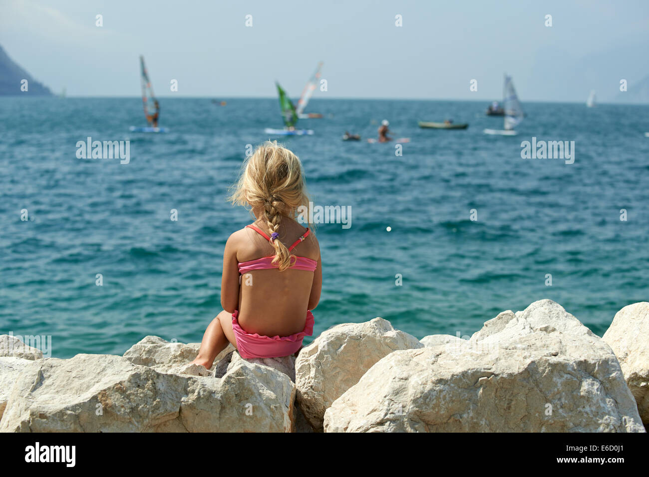 Child blond girl looks at Windsurfers on Lake Garda near Torbole ...