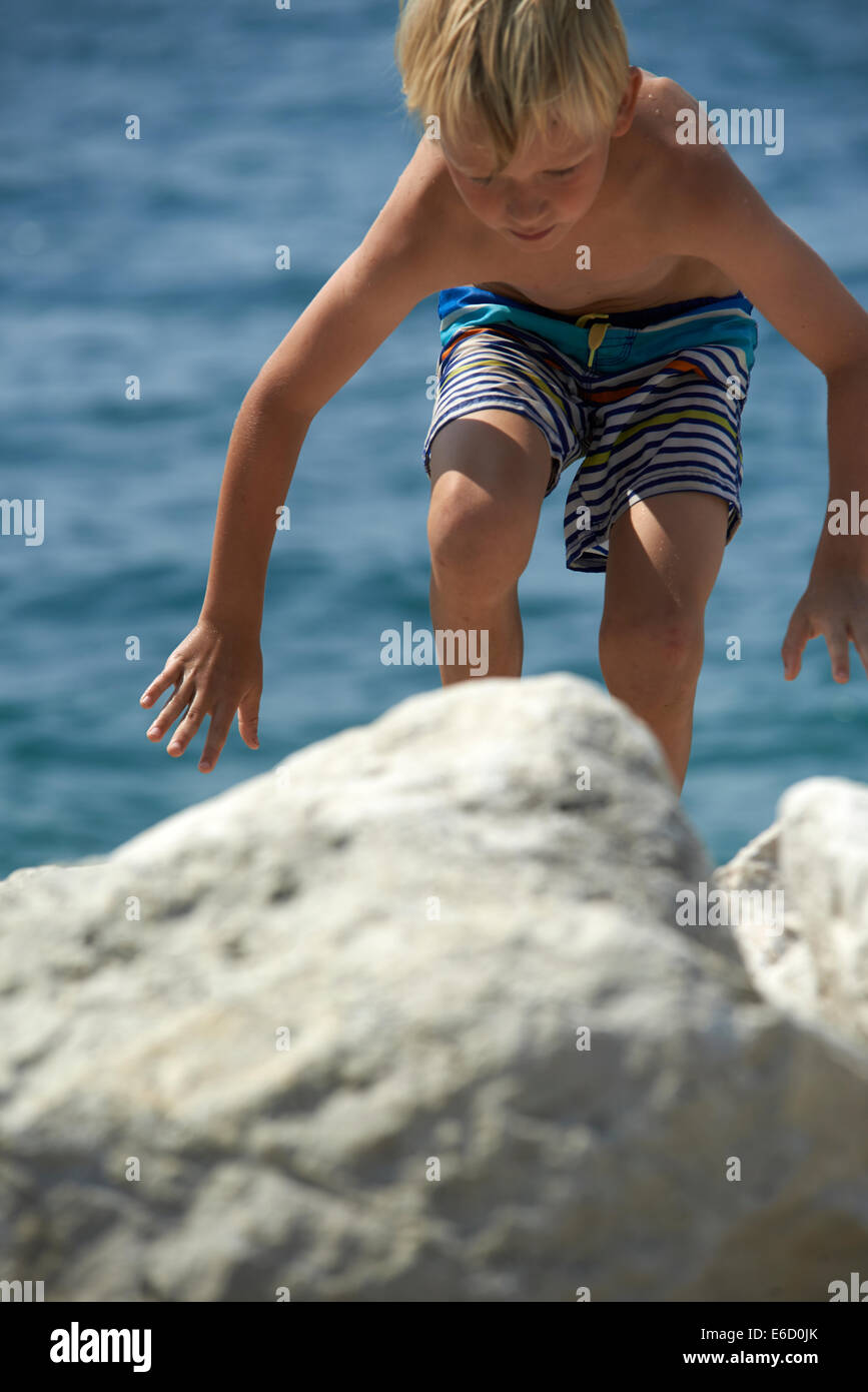 Child Blond Boy Climbing Rock by Sea summer beach Stock Photo