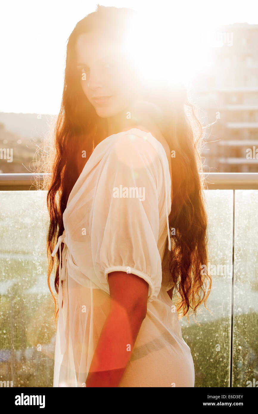 Young confident woman in her 20s with long brown hair in casual white dress. Backlit by the sun. Model release available Stock Photo