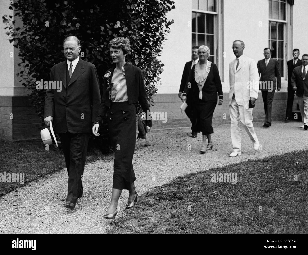 Vintage photo of American aviation pioneer and author Amelia Earhart (1897 – declared dead 1939) – Earhart and her navigator Fred Noonan famously vanished in 1937 while she was trying to become the first female to complete a circumnavigational flight of the globe. Earhart is pictured walking with President Herbert Hoover at The White House in June 1932 where Hoover presented her with a National Geographic Society gold medal in recognition of her non-stop solo flight across the Atlantic. Stock Photo