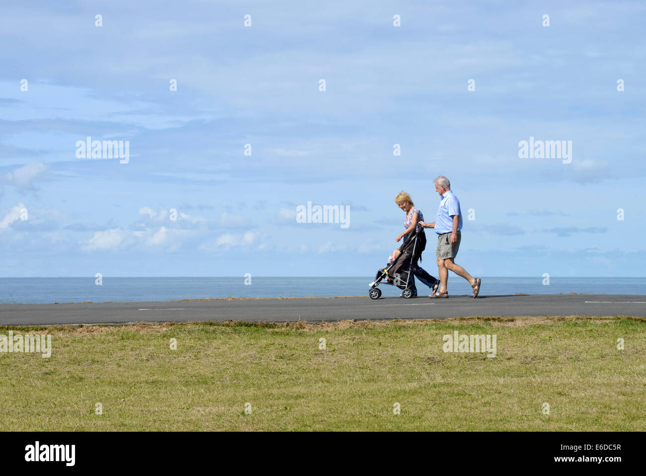Older couple pushing child in pushchair (stroller) on coastal path in Blackpool, Lancashire Stock Photo