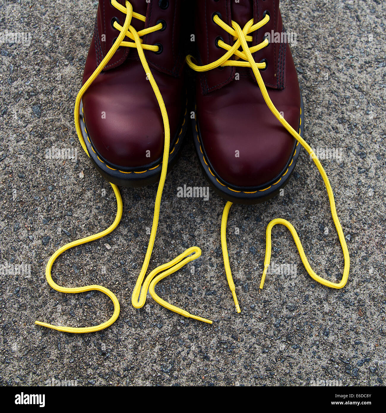 Red Dr Martens boots with yellow laces spelling Skin on paving stone Stock Photo
