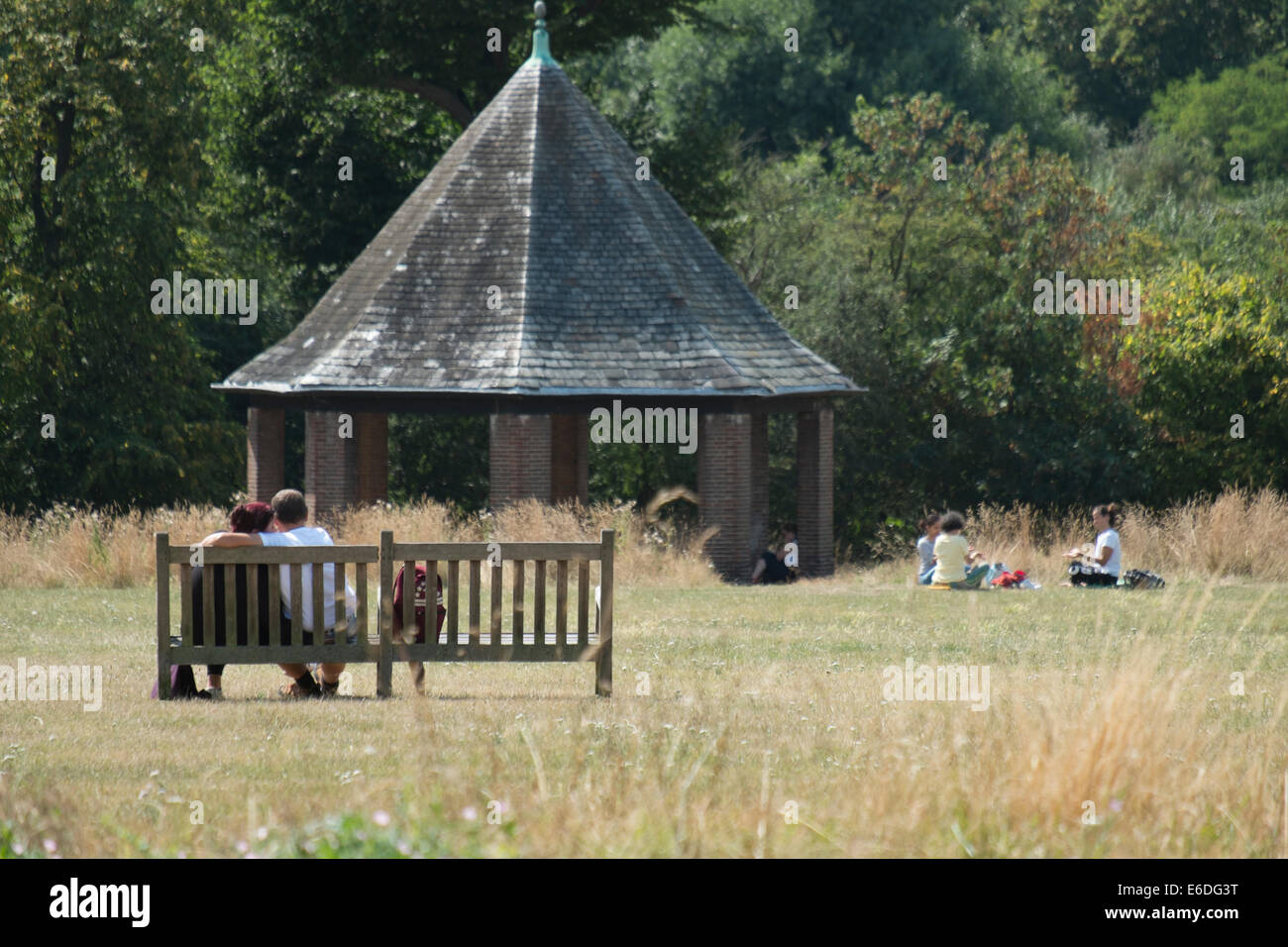 Couple on a bench with family in the background on a warm summers day in London's Hyde Park Stock Photo