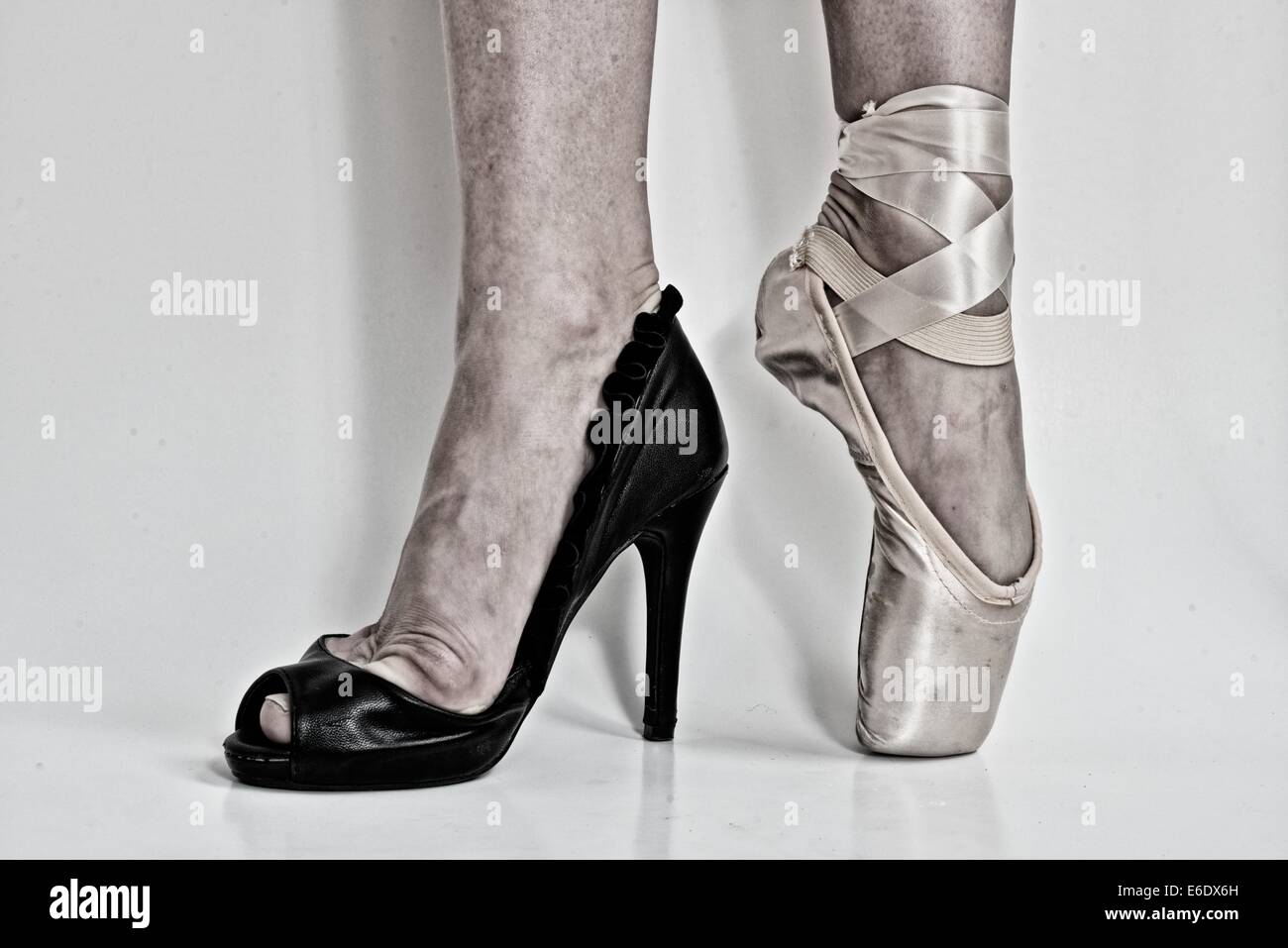 Legs of a ballerina with a black high heel shoe in one feet and a pointe ballet shoe in the other. Stock Photo