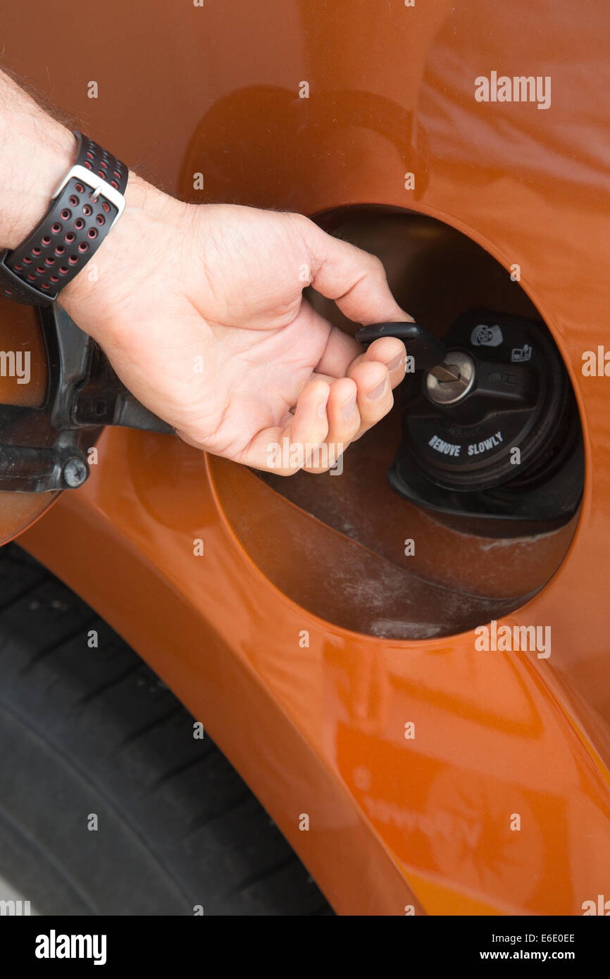 Man's hand unlocking an antitheft vehicle fuel cap with key at a gas station Stock Photo
