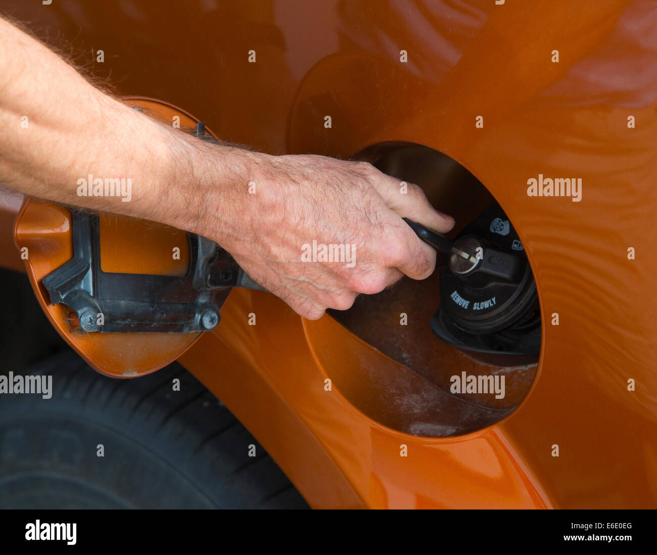 Man's hand unlocking an antitheft vehicle fuel cap with key at a gas station Stock Photo