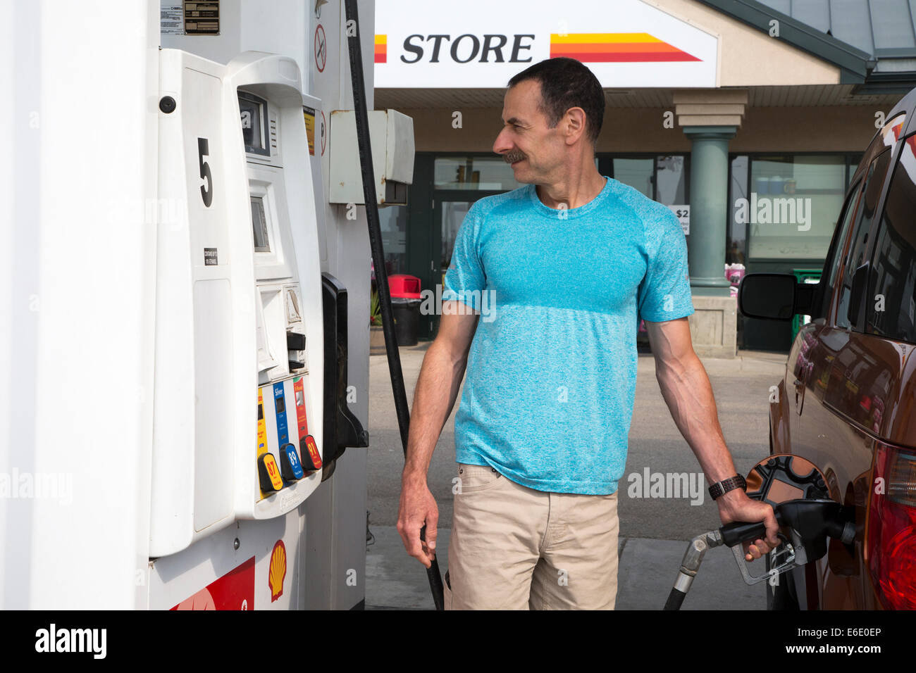 Man pumping gas into his vehicle while watching the price display at a service station in Alberta, Canada Stock Photo