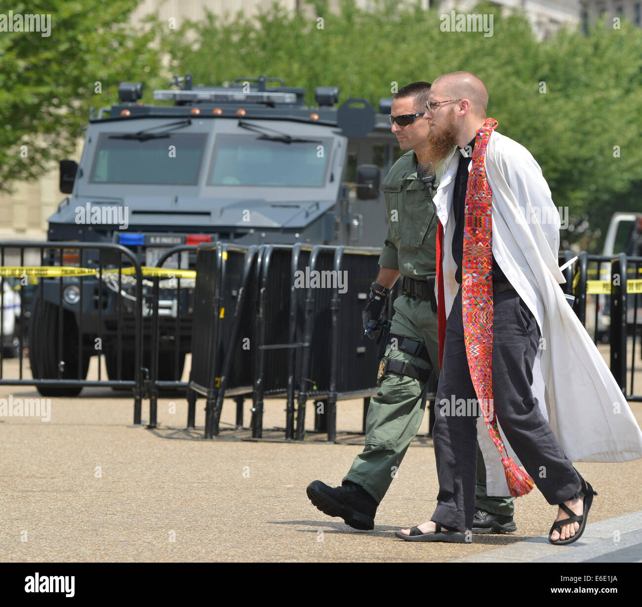 Washington, DC, USA. 31st July, 2014. The Rev. Jeffrey K. Hood, a Baptist pastor from Texas, is arrested in front of the White House during an immigration protest that also included faith leaders from the United Methodist Church, Catholics, Unitarian Universalists, Quakers, Jews, and others. Although the faith leaders cooperated with U.S. Park Police and notified them in advance of the peaceable protest and their intention to be arrested, the police response included a military-style 'BearCat'' armored personnel carrier, seen in the background. Police use of such equipment in Ferguson, Mis Stock Photo