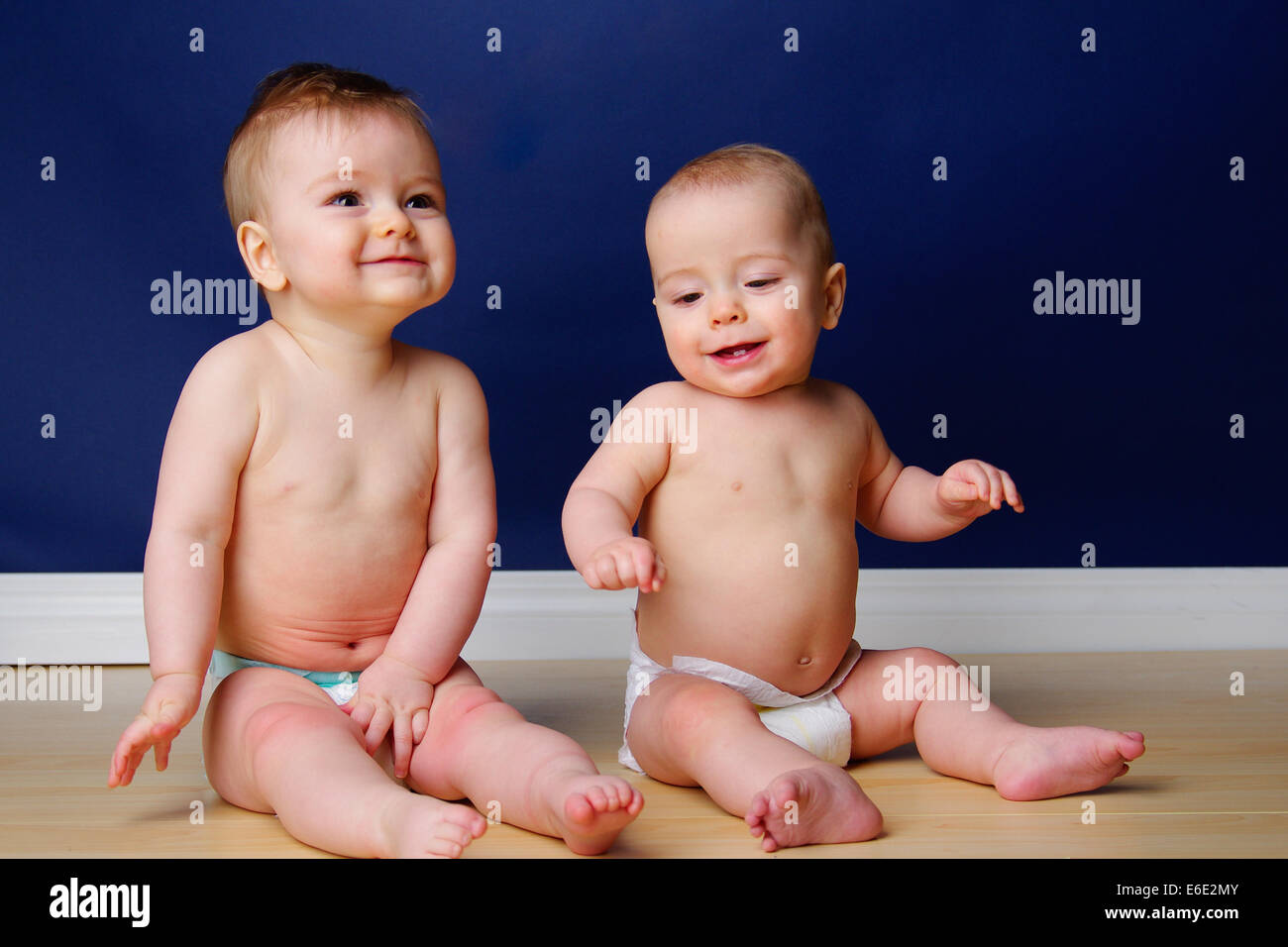 Twin 9 month old babies grinning and sitting up Stock Photo
