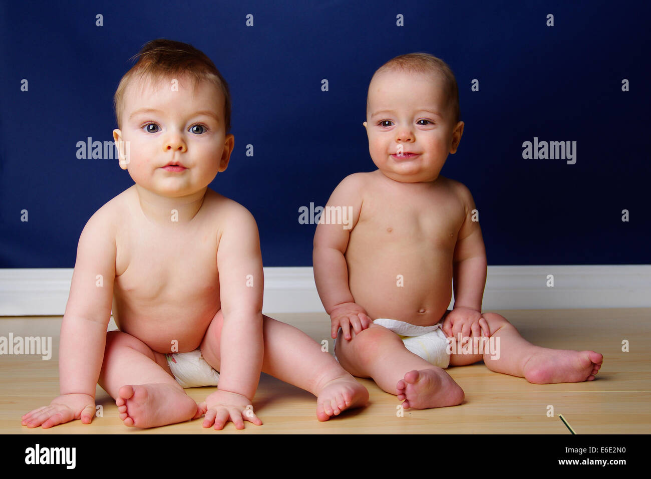 Fraternal twin 9 month old baby boys sitting side by side in their diapers Stock Photo