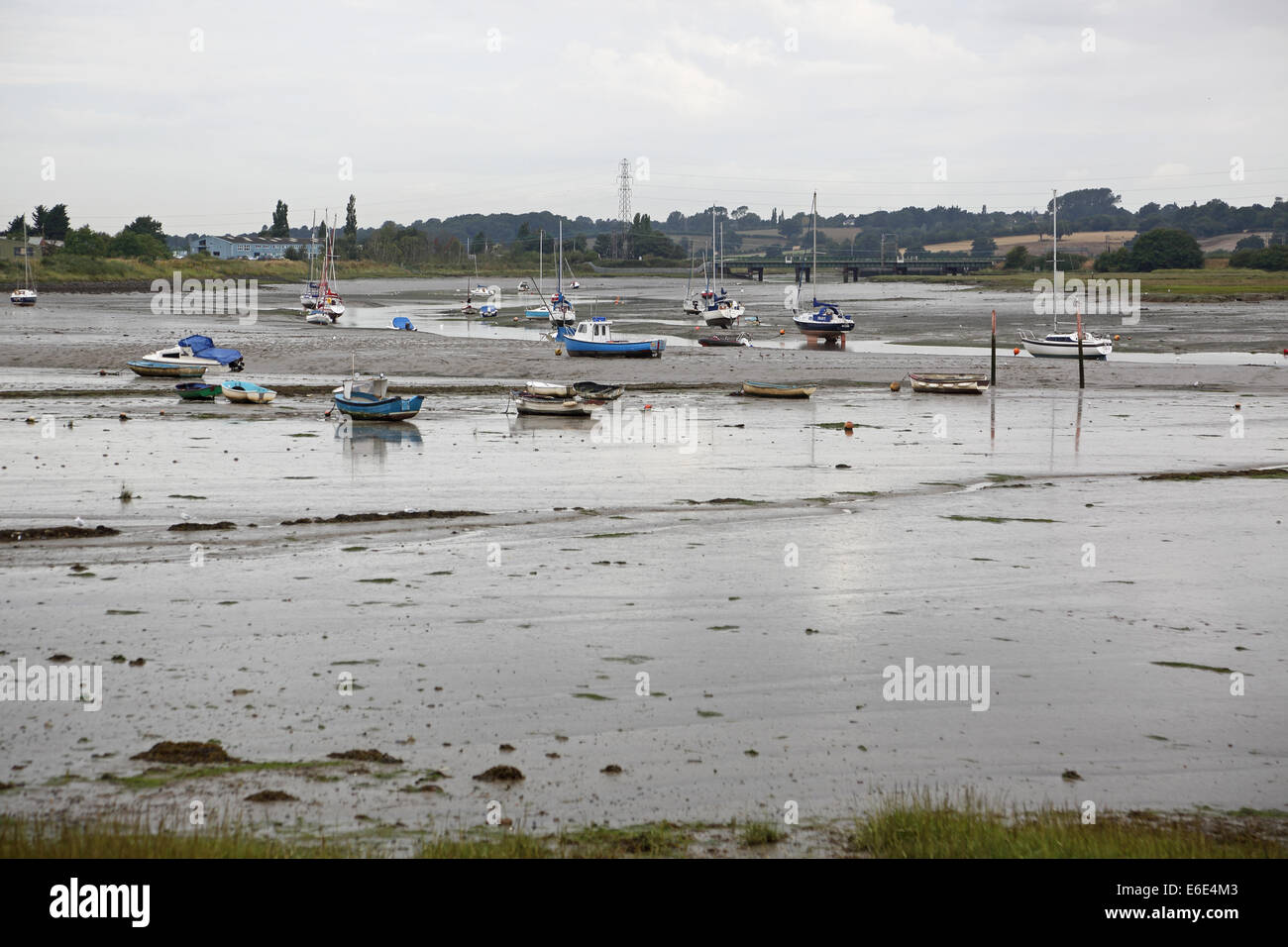 The River Stour estuary, Essex, UK, at low tide showing mud flats and moored yachts. Railway bridge in distance. Stock Photo