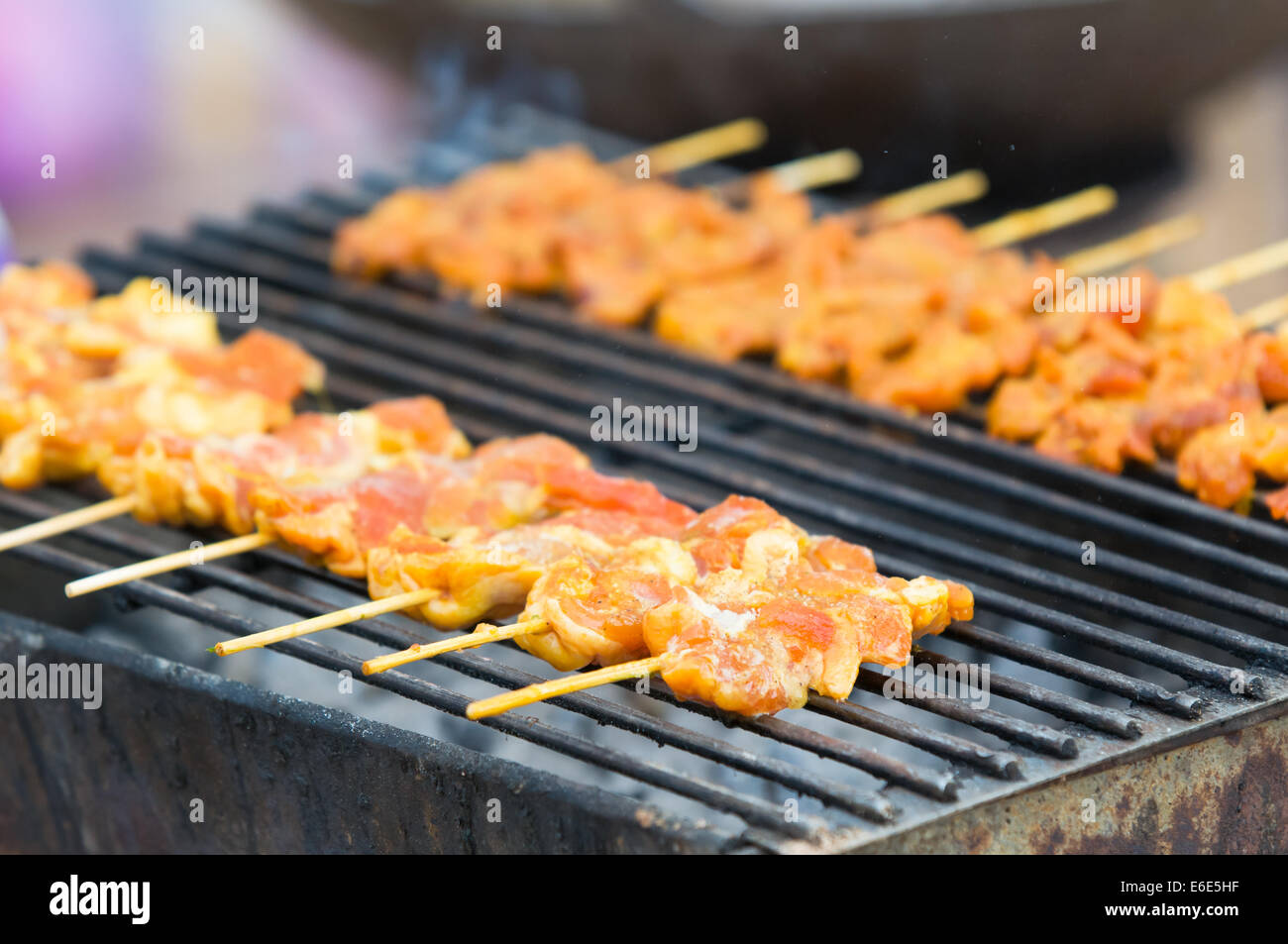 Pieces of pork on wooden sticks on a barbecue in Thailand. Very shallow depth of field with the nearest pieces of pork in focus. Stock Photo
