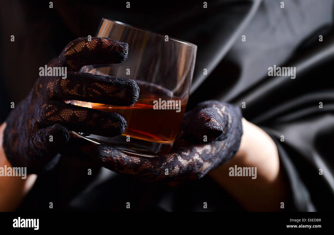 woman in black gloves with glass of whiskey Stock Photo