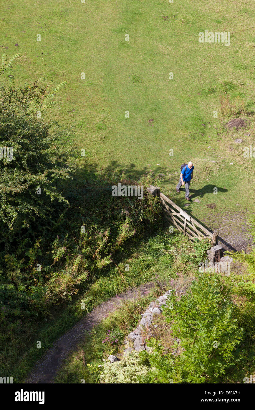 Hiking in the countryside. A hiker walking towards a gate in a field seen from above. Derbyshire, Peak District, England, UK Stock Photo