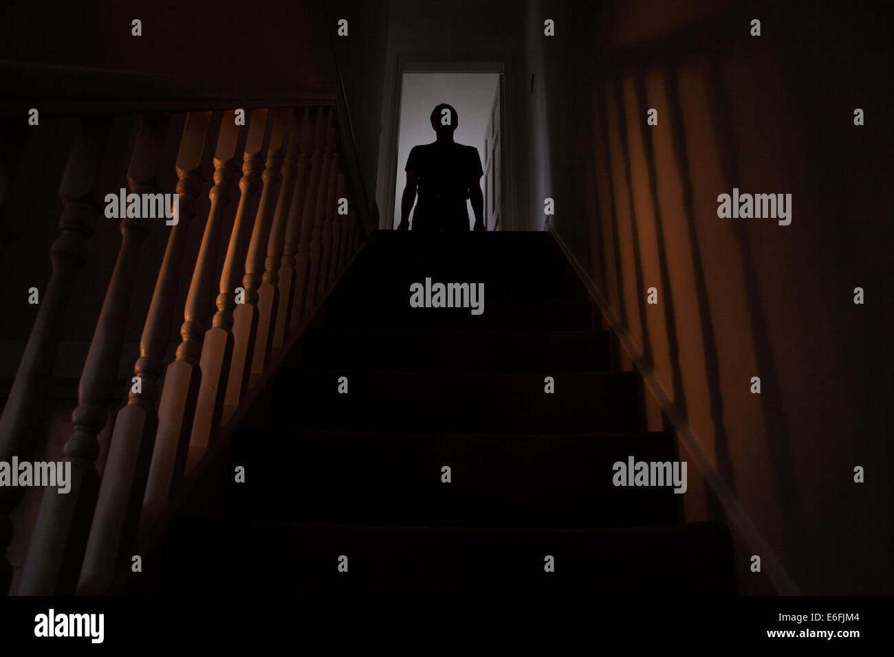 Silhouette of a man standing at the top of a stairway, shadows cast on the walls from the light below. Stock Photo