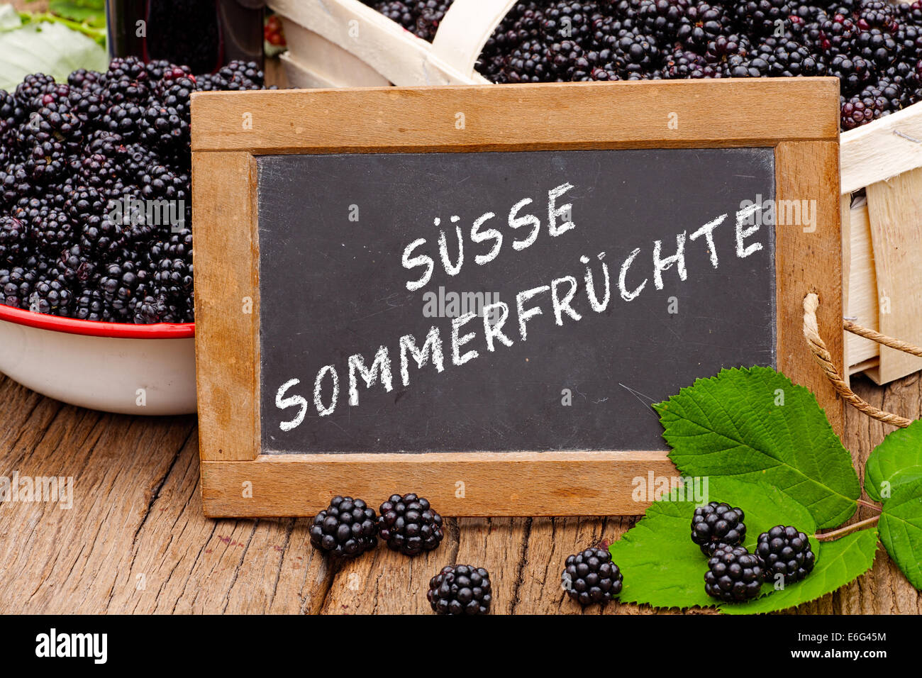 Slate blackboard with the Germans words: Suesse Sommerfruechte (Sweet Summer fruits), in front of ripe blackberries Stock Photo